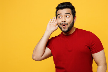 Young curious nosy happy Indian man he wearing red t-shirt casual clothes trying to hear you...