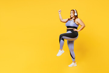 Fototapeta na wymiar Full body young plus size big fat fit woman wear blue top warm up training listen to music in headphones raise up leg hand isolated on plain yellow background studio home gym. Workout sport concept.