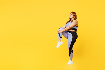 Fototapeta na wymiar Full body side view young chubby plus size big fat fit woman wear blue top warm up training raise up leg do stretch exercises isolated on plain yellow background studio home gym Workout sport concept