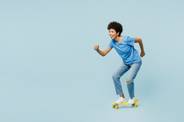 Full body side profile view young woman of African American ethnicity wears t-shirt casual clothes riding skateboard pennyboard isolated on plain pastel light blue cyan background. Lifestyle concept.