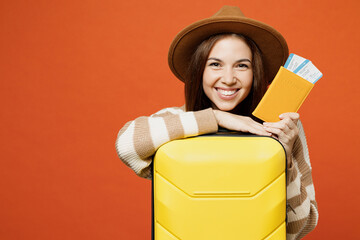 Traveler smiling woman wear brown sweater hat hold bag passport ticket isolated on plain orange red...