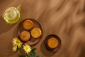 Over the brown background, two wooden dishes are featured few baked mooncakes. A pot of warm tea...