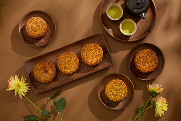 A set of tea in black color and several tasty mooncakes are arranged on round and rectangle dishes. Brown background. Background food and drink tea and Mooncakes