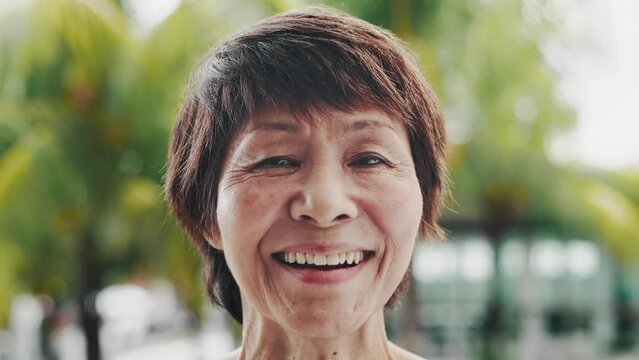 Portrait of Adult Asian Woman Looking at Camera Close Up. Head Shot or Front View of Old Japanese or Chinese Female Posing on Green Background. Joyful Life Time and Diverse Culture of Aged Asia People