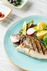 Grilled sea bream with vegetables and greens on wooden table