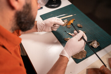 Close-up of male working at office at night restoring ancient coins, top view. Archaeological