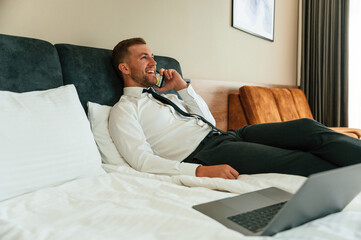 Fototapeta premium Talking by phone. Businessman is indoors in the hotel room