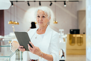 Portrait of senior business woman holding digital tablet while standing at jewelry store....