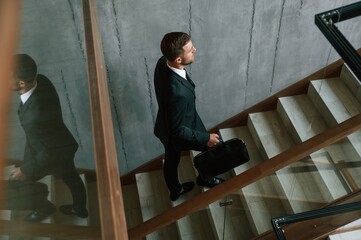 Walking up. Man in business suit and tie with case in hands is on the stairs