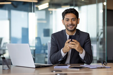 Portrait of young hispanic worker, businessman smiling and looking at camera at workplace inside...