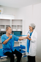 Fototapeta premium Asian physiotherapist helping elderly man patient stretching arm during exercise correct with dumbbell in hand during training hand in bed in clinic