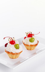 Beautiful cream cakes with cherries and grapes on a plate on a white background