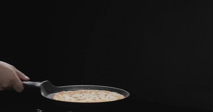 Close-up shot of flipping pancakes over black background. Slow motion