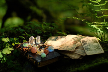 witch book with set of minerals, divination cards close up in forest, abstract blurred natural...