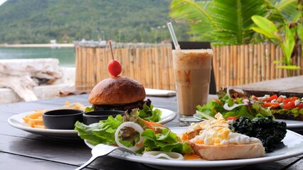Man drink iced cocktail, enjoying vegan food by ocean. Close-up menu of vegan food in cafe poached eggs, salad, healthy burger, avocado toast, cocktail. Concept visit cafe to enjoy healthy vegan food.