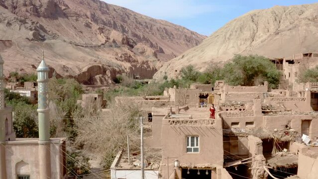 Young woman in red dress walking on mud house rooftop in Tuyoq rural Chinese village. Aerial