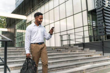 With purpose in his stride, the stylish African-American businessman carries his laptop bag and holds his phone, ready to conquer the day's challenges.