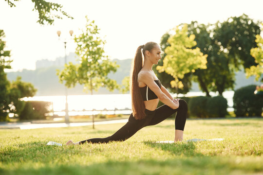 Doing squats. Beautiful young woman in sportive clothes is in the park at sunny daytime