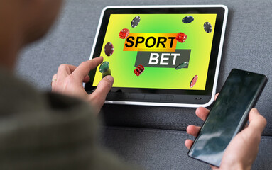 Lucky man celebrating victory after making bets using gambling mobile application on his phone. Football match online broadcast on laptop screen on the background.