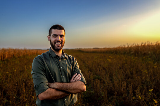 Portrait of young farmer standing in a soy field at sunset looking at camera.
