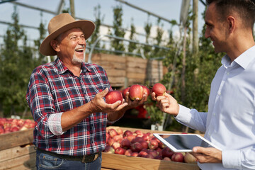 Senior farmer and sales representative talking over digital tablet on apple orchard