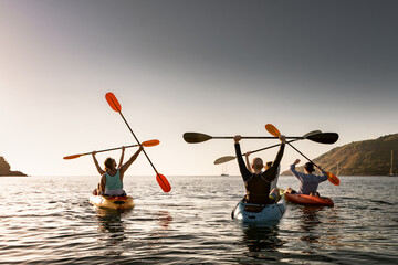 Group of young happy kayakers are having fun in winner poses at sunset sea bay