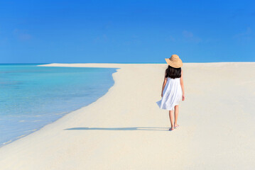 Back of young Asian girl walking on white sand beach with clear blue sea and sky. Teenager girl...