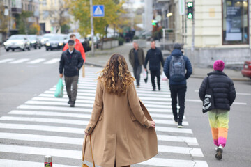 A girl in a beige coat and a red handbag crosses the pedestrian crossing on the road. Europe. autumn Fashion concept