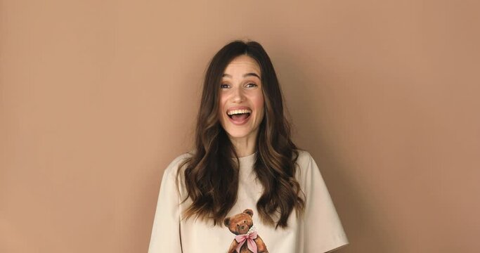 Happy friendly brunette woman waves palm in hello gesture welcomes someone with hospitable expression expresses positive emotions dressed casually isolated over beige background. Hi to all of you.