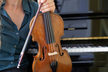 Fototapeta premium Frau hält Geige in Hand mit Klavier im Hintergrund. Woman holding violin in hand with piano in background.