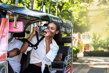 Young black independent tourist sitting in tuktuk and taking photoes during summer vacation in...