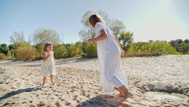 Mom and daughter in white dresses running on the beach and laughing