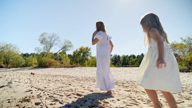 Mom and daughter in white dresses running on the beach and laughing