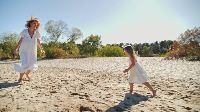 Mom and daughter in white dresses running on the beach and laughing