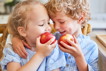 Two happy children eating apples in kitchen