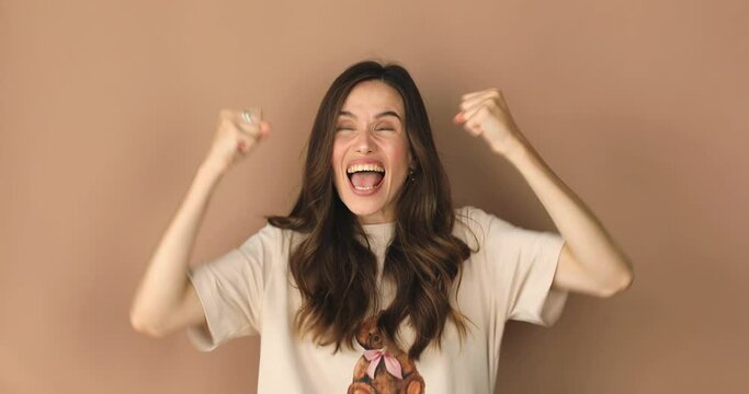 Excited sport fan young woman in beige t-shirt wait for special moment go celebrate win scream rejoices doing winner hands gesture at last isolated on beige color wall background.