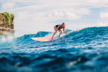 Blonde surf girl riding on surfboard in ocean during surfing. Surfer on blue wave
