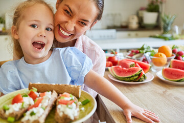 Happy mother with daughter holding food plate at home