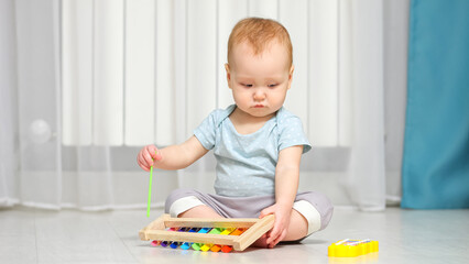 Baby girl plays around with xylophone toy on floor in house. Small child in ordinary clothes learning to play music using colorful toys