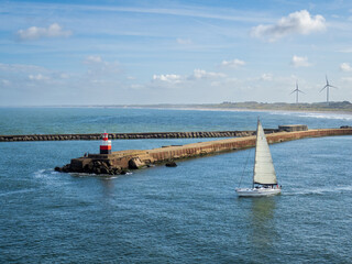 Sailing yacht setting out to sea on a sunny day passing the breakwater and lighthouse