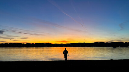 Human silhouette at sunset looking into the distance beyond the horizon of the lake.