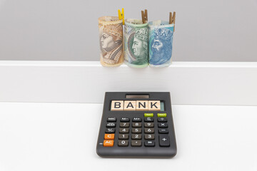 Banknotes arranged in a roll of 3 denominations of 50 zloty 100 zloty and 200 zloty next to which lies a wooden Bank sign on a calculator. The concept of spending during a crisis of inflation and rece