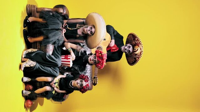 Young man, woman, daughters in sugar skull makeup and costumes watching horror movie on yellow background. Concept of halloween, El Dia de Muertos, holidays and festivals, mexican traditions, family