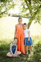 beautiful woman , mother with orange dress with her two daughters outdoor in the nature