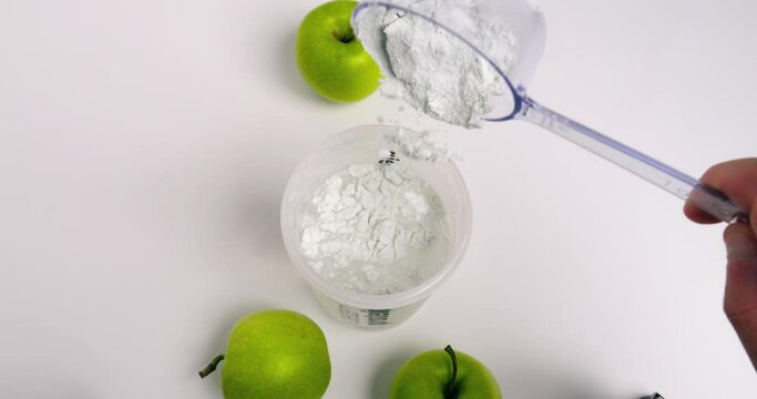 Birdseye static shot from a shaker filled with water while adding a scoop of finest green apple whey powder for a tasty shake with green apples on the side