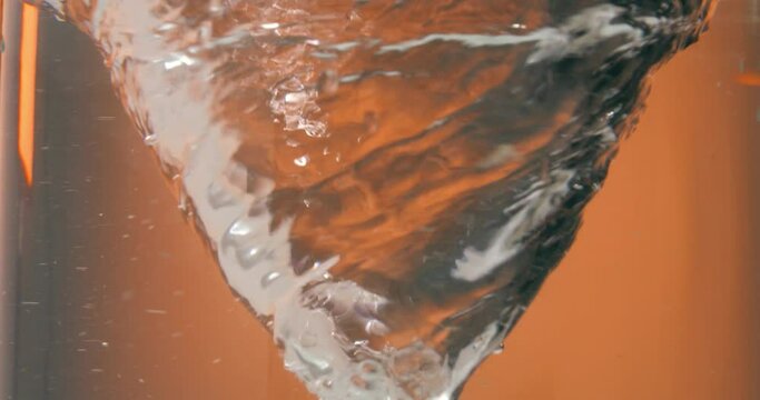 Static slow motion shot of a spinning or circling water vortex or water tornado in front of orange background