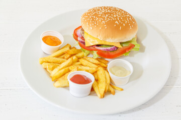 Burger avec des frites sur une assiete et fond blanc avec des différentes sauces. Restauration rapide.