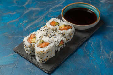 California rolls au saumon sur une ardoise avec une sauje soja et baguettes. Cusine japonaise.