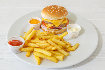 Burger avec des frites sur une assiete et fond blanc avec des différentes sauces. Restauration rapide.