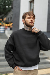 Stylish handsome young hipster man with a hairstyle and beard with a tattoo in a black fashionable...
